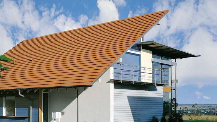 Modernes Einfamilienhaus mit rotem Satteldach, großen Fenstern und Balkonen, umgeben von einem gepflegten Garten.