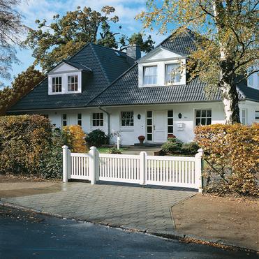 Elegantes zweigeschossiges Haus mit Satteldach, umgeben von Garten und weißem Zaun. Großer Eingangsbereich sichtbar.