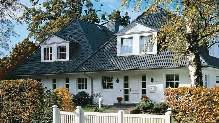 Elegantes zweigeschossiges Haus mit Satteldach, umgeben von Garten und weißem Zaun. Großer Eingangsbereich sichtbar.