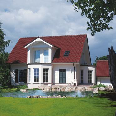 Helles modernes Haus mit rotem Dach, umgeben von Grün und einem kleinen Teich mit Steinen im Vordergrund.