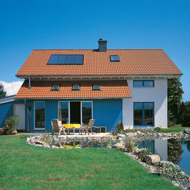 Moderne zweigeschossige Wohnhausfassade mit blauer Holzverkleidung, Terrassensitzgruppe und angrenzendem Teich im Garten.