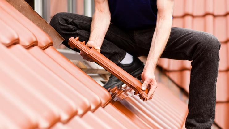Handwerker platziert einen Dachziegel auf einem geneigten, roten Ziegeldach.