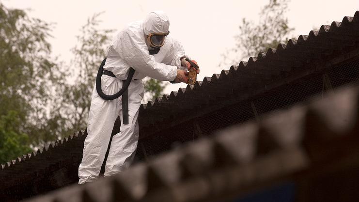 Arbeiter in Schutzanzug verwendet eine elektrische Säge zur Reparatur eines Daches bei bewölktem Wetter.